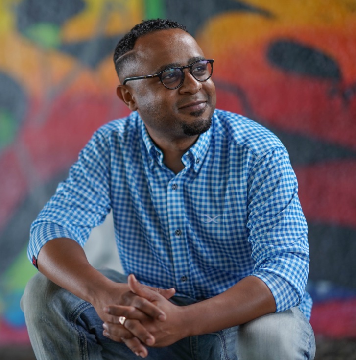 Yannick Bashizi, assis devant un mur coloré